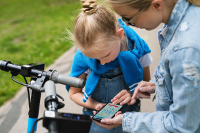 mother daughter using application smartphone sharing electric scooters city park 